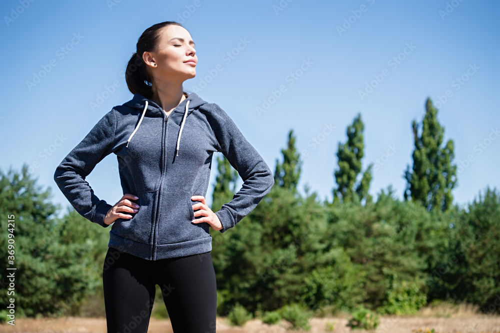 Young woman exercising stretching in sports outfit on a natural meadow with trees and blue sky in the background Young woman exercising stretching in sports outfit on a natural meadow with trees and blue sky in the background