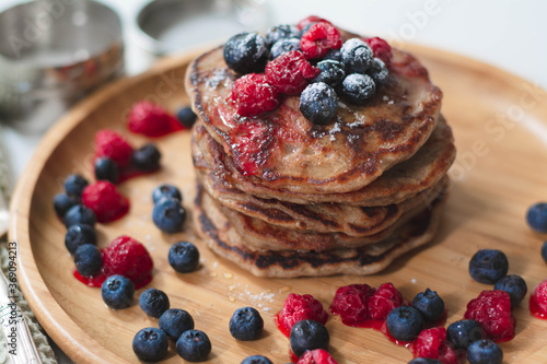 A heap of healthy vegan gluten-free whole grain pancakes made with buckwheat flour topped with raspberries and blueberries with icing sugar sprinkled on top 