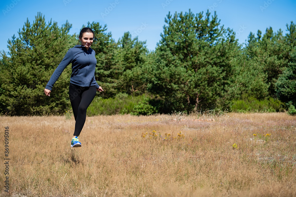 Young woman running on a natural meadow in the background of green trees and blue sky Young woman running on a natural meadow in the background of green trees and blue sky