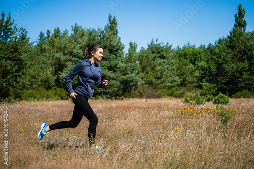 Young woman running on a natural meadow in the background of green trees and blue sky