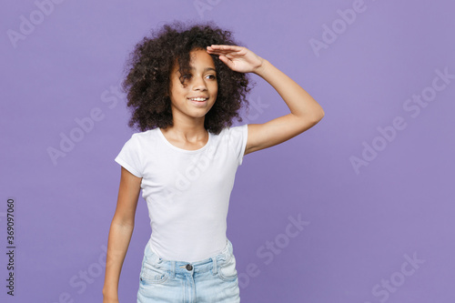 Little african american kid girl 12-13 years old in white t-shirt isolated on violet background. Childhood lifestyle concept. Mock up copy space. Holding hand at forehead looking far away distance.