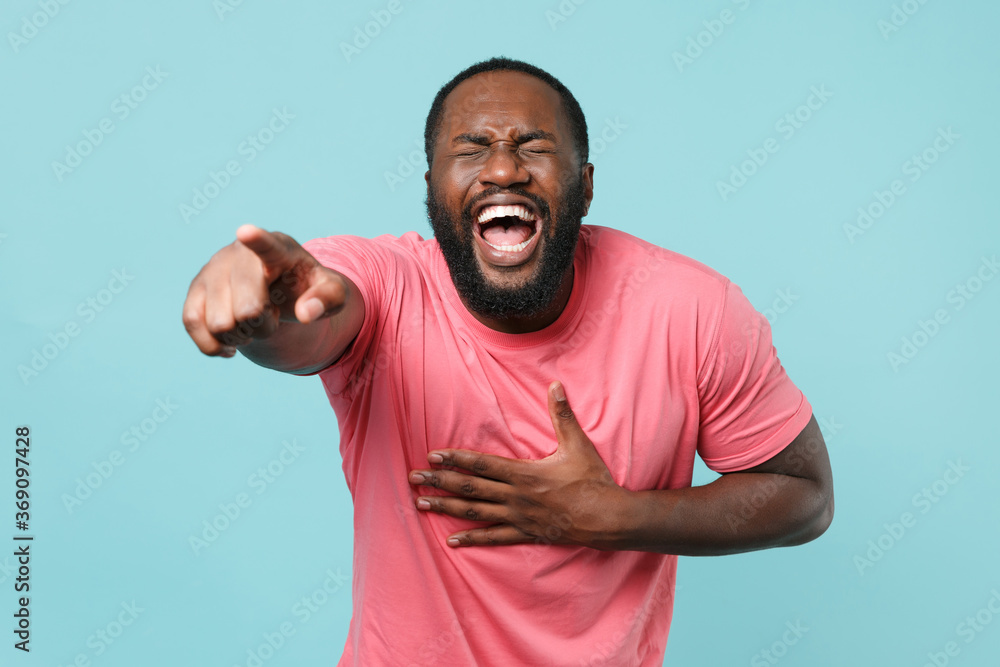 Laughing young african american man guy in casual pink t-shirt posing isolated on blue background. People lifestyle concept. Mock up copy space. Pointing index finger on camera, put hand on stomach. Laughing young african american man guy in casual pink t-shirt posing isolated on blue background. People lifestyle concept. Mock up copy space. Pointing index finger on camera, put hand on stomach.