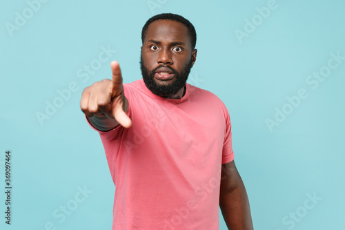 Shocked displeased young african american man guy in casual pink t-shirt posing isolated on blue background studio portrait. People lifestyle concept. Mock up copy space. Point index finger on camera.