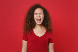 Frustrated young african american woman girl in casual t-shirt posing isolated on red background studio portrait. People emotions lifestyle concept. Mock up copy space. Keeping eyes closed, screaming.