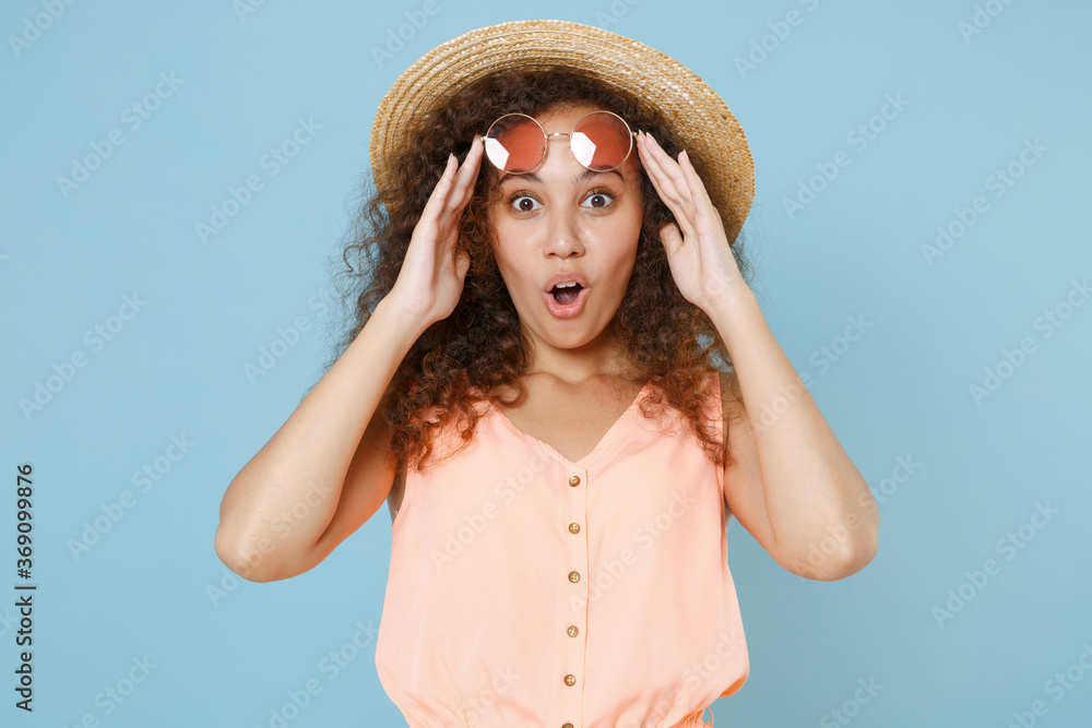 Shocked young african american girl in pastel summer clothes hat glasses isolated on blue background studio portrait. People sincere emotions lifestyle concept. Mock up copy space. Keeping mouth open. Shocked young african american girl in pastel summer clothes hat glasses isolated on blue background studio portrait. People sincere emotions lifestyle concept. Mock up copy space. Keeping mouth open.
