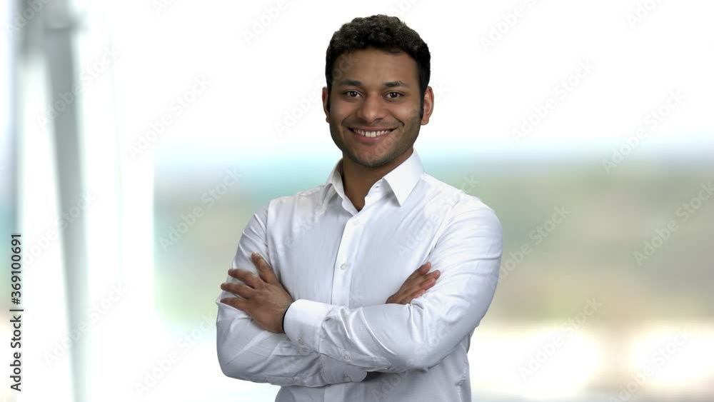 Smiling dark-skinned man on blurred background. Attractive Indian executive in white shirt looking at camera with folded arms. Smiling dark-skinned man on blurred background. Attractive Indian executive in white shirt looking at camera with folded arms.