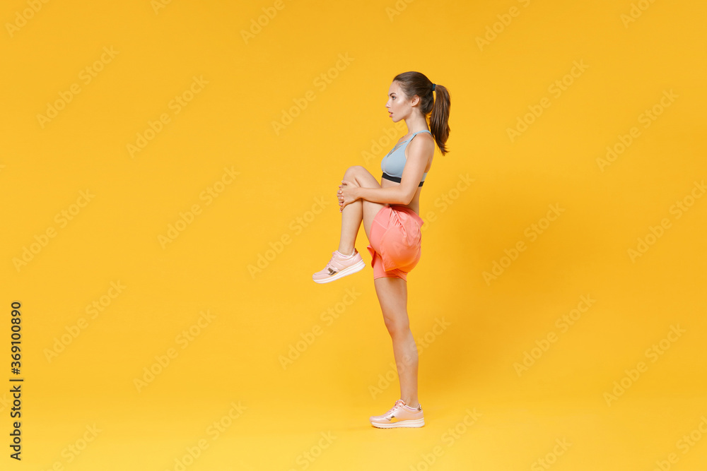 Full length portrait strong fitness woman in sportswear working out isolated on yellow background. Workout sport motivation lifestyle concept. Mock up copy space. Doing stretching exercising for legs. - obrazy, fototapety, plakaty 