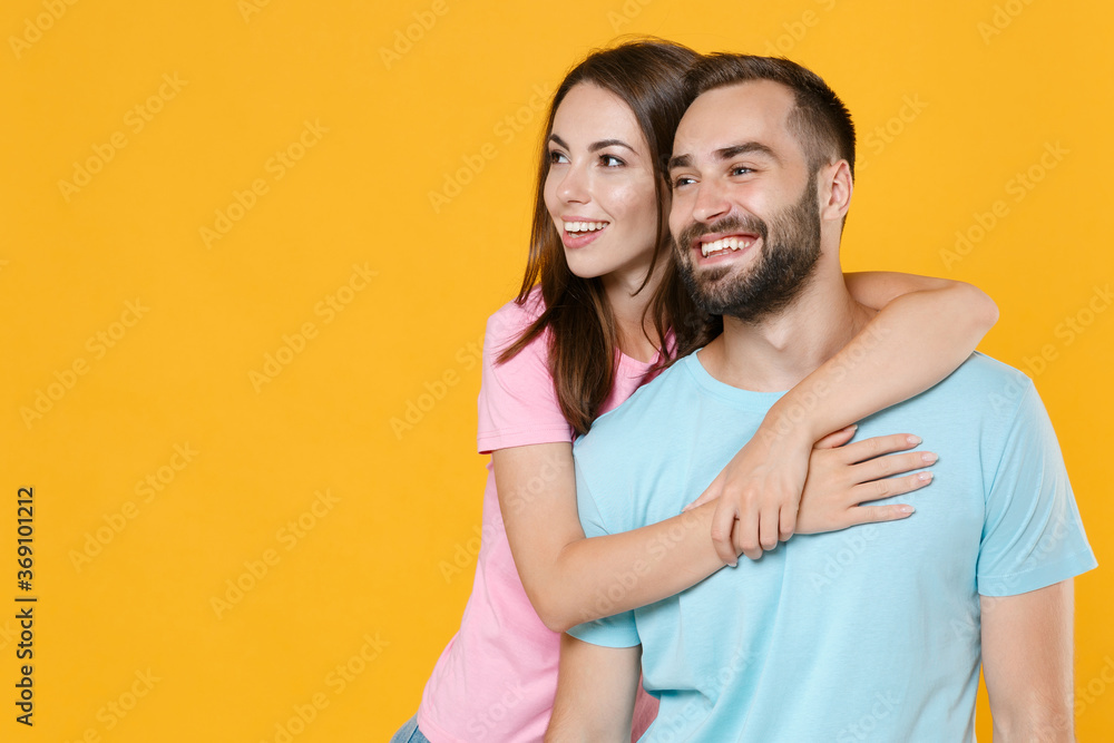 Naklejka premium Smiling young couple friends guy girl in blue pink t-shirts posing isolated on yellow wall background studio portrait. People emotions lifestyle concept. Mock up copy space. Hugging, looking aside.