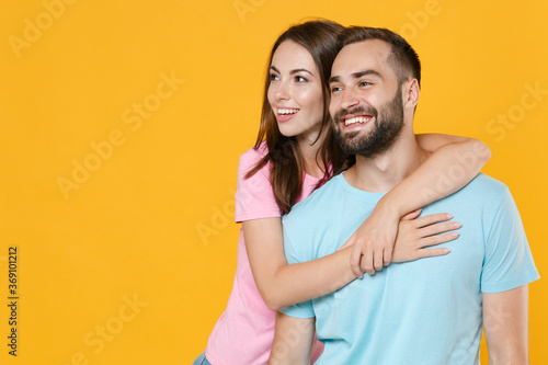 Smiling young couple friends guy girl in blue pink t-shirts posing isolated on yellow wall background studio portrait. People emotions lifestyle concept. Mock up copy space. Hugging, looking aside.