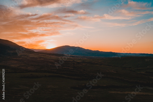 Carpathian meadow and beautiful sunset in the mountains - spring landscape, spruces on the hills, dark cloudy sky and bright sunlight, the village can be seen on the horizon.