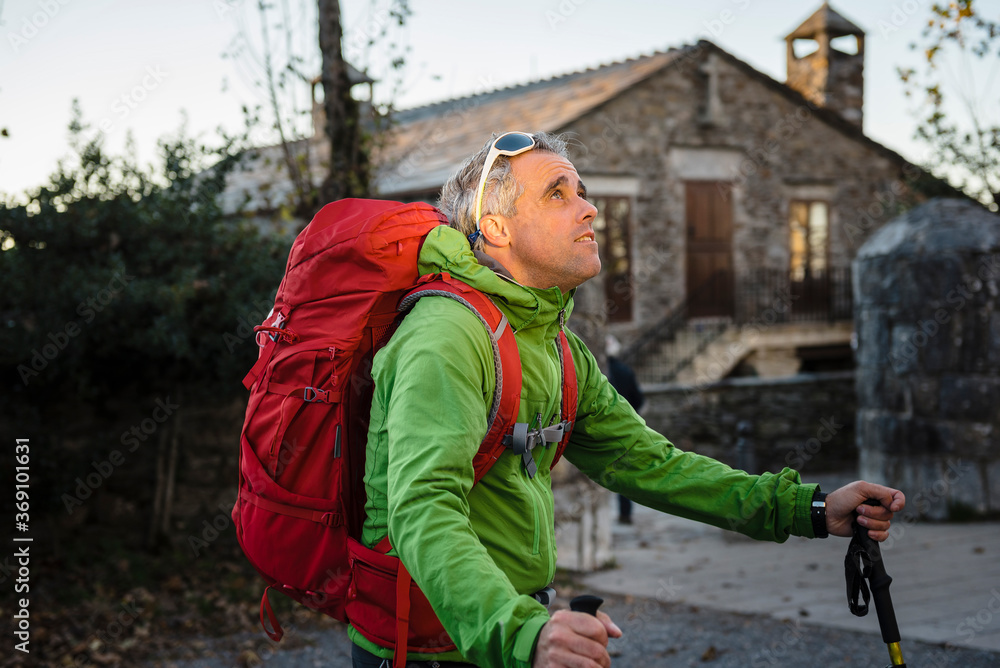 MIddle age pilgrim holding backpack in Saint Jame´s Way with church on background MIddle age pilgrim holding backpack in Saint Jame´s Way with church on background