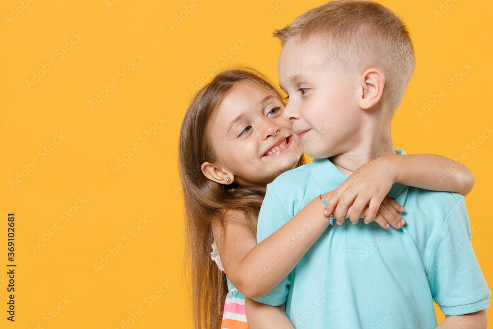 Little couple kids boy girl 5-6 years old in blue pink clothes shirt dress posing have fun isolated on yellow background children studio portrait. People childhood lifestyle concept embrace hug love