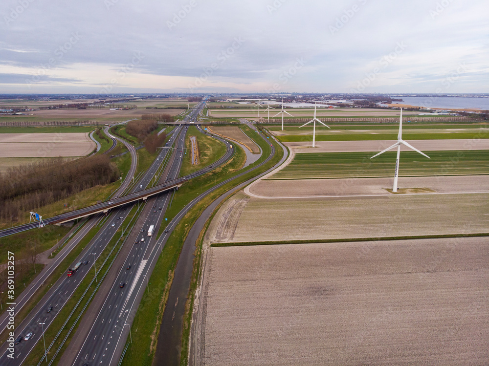 Row of wind turbines in The Netherlands at Cloudy day on an Amsterdam - Rotterdam vehicle highway