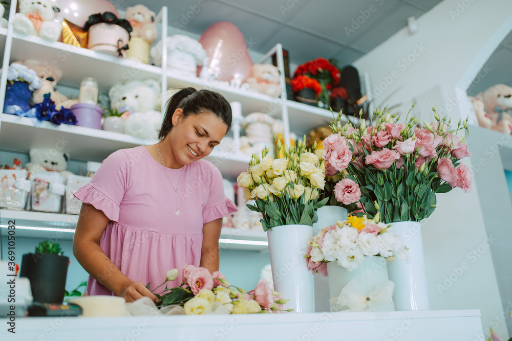 Young attractive brunette caucasian woman florist in a pink dress arranging a bouquet of flowers in a flower shop Young attractive brunette caucasian woman florist in a pink dress arranging a bouquet of flowers in a flower shop