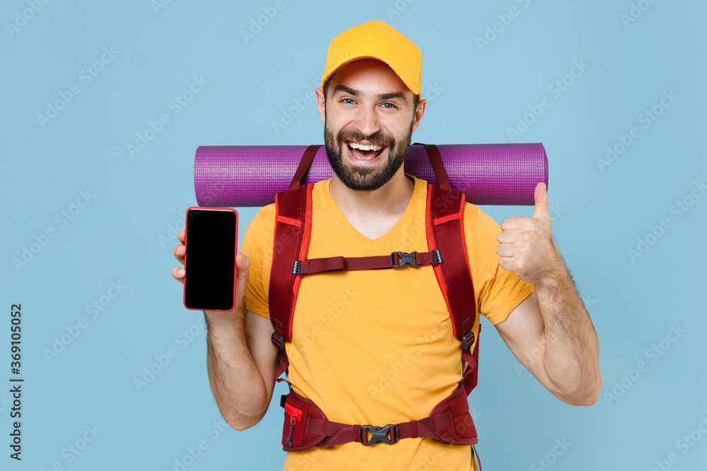 Funny traveler man with backpack isolated on blue background. Tourist traveling on weekend. Tourism discovering hiking concept. Mock up copy space Hold mobile phone with blank screen showing thumb up. Funny traveler man with backpack isolated on blue background. Tourist traveling on weekend. Tourism discovering hiking concept. Mock up copy space Hold mobile phone with blank screen showing thumb up.