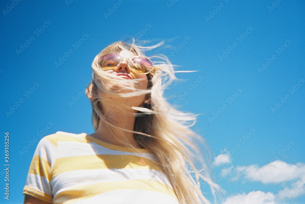 © wendy laurel/Stocksy - Blonde beautiful woman against bright blue sky in underwear and bra and striped tee