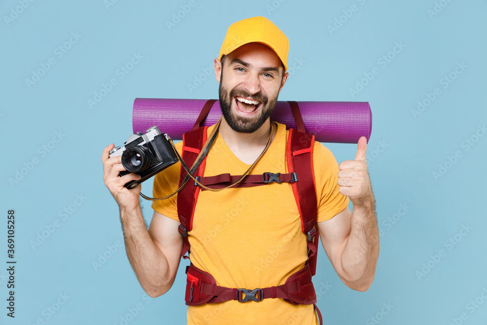 Cheerful young traveler man in t-shirt backpack isolated on blue background. Tourist traveling on weekend getaway. Tourism discovering hiking concept. Hold retro vintage photo camera showing thumb up. Cheerful young traveler man in t-shirt backpack isolated on blue background. Tourist traveling on weekend getaway. Tourism discovering hiking concept. Hold retro vintage photo camera showing thumb up.