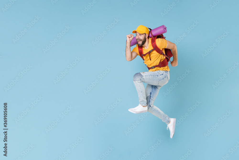 Full length portrait Excited young traveler man in cap with backpack isolated on blue wall background. Tourist traveling on weekend getaway. Tourism discovering hiking concept. Jumping like running. Full length portrait Excited young traveler man in cap with backpack isolated on blue wall background. Tourist traveling on weekend getaway. Tourism discovering hiking concept. Jumping like running.