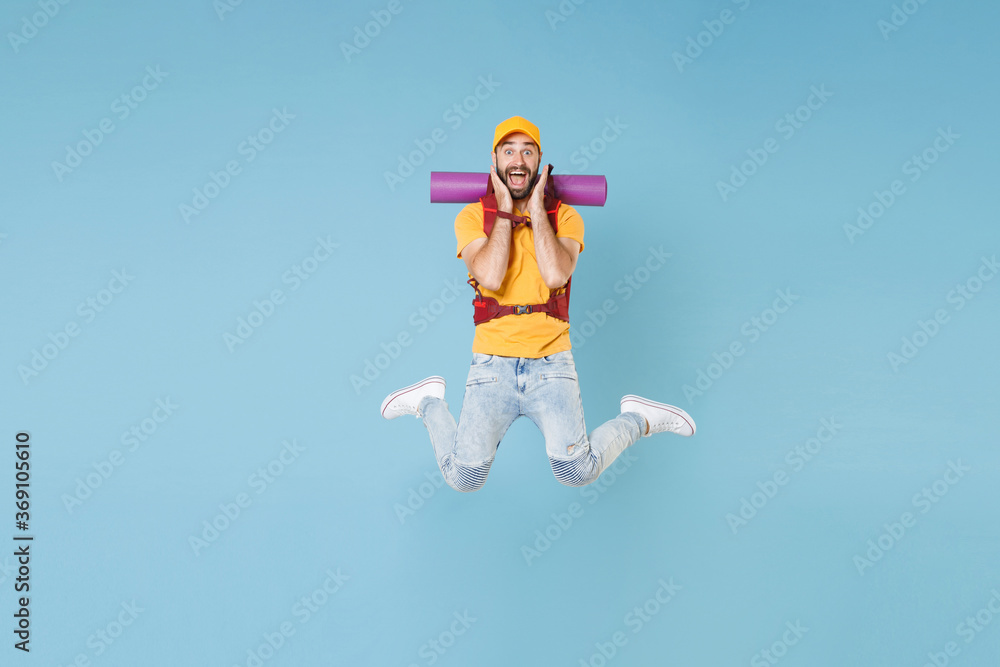 Full length portrait Excited young traveler man in t-shirt cap backpack isolated on blue background. Tourist traveling on weekend getaway. Tourism discovering hiking concept. Jump put hands on cheeks.