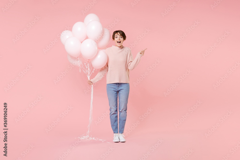 Full length portrait of shocked young girl in casual sweater isolated on pink background. Birthday holiday party concept. Mock up copy space. Celebrating hold air balloons pointing index finger aside. Full length portrait of shocked young girl in casual sweater isolated on pink background. Birthday holiday party concept. Mock up copy space. Celebrating hold air balloons pointing index finger aside.