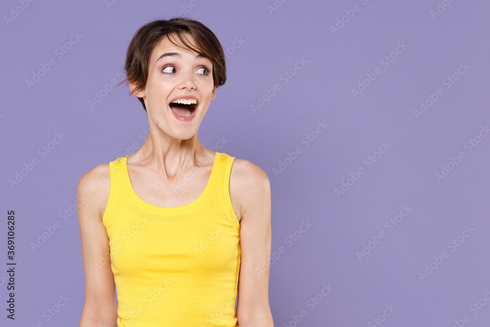 Excited young brunette woman girl in yellow casual tank top posing isolated on pastel violet background studio portrait. People sincere emotions lifestyle concept. Keeping mouth open, looking aside. Excited young brunette woman girl in yellow casual tank top posing isolated on pastel violet background studio portrait. People sincere emotions lifestyle concept. Keeping mouth open, looking aside.