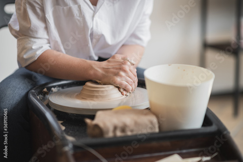 Close-up view of woman hands working on pottery wheel and making clay pot. Hands sculpts a cup from clay pot. Workshop on modeling on the potter's wheel