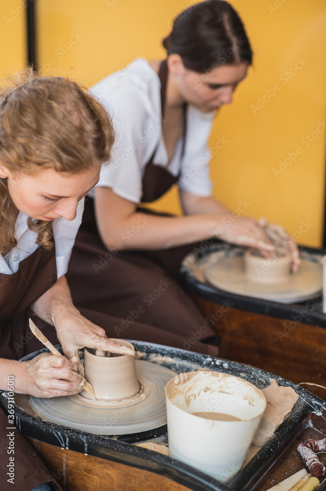 Overview of two young potters by pottery wheels while preparing ceramic pots from raw clay. Overview of two young potters by pottery wheels while preparing ceramic pots from raw clay.
