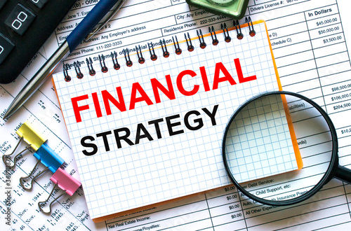 Text Financial Strategy on notepad with calculator, clips, pen on financial report
