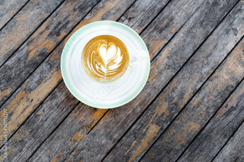 Cup of fresh creamy cappuccino with latte art on foam. Background of wooden table with shabby aged surface. Directly from above.