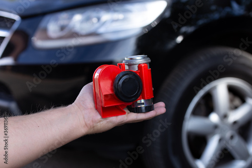 Red air horn for a car on men's hand before a modern black car.