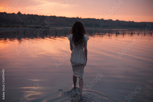 girl in a dress walks in the sunset water