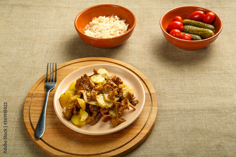 potatoes with mushrooms larvae on a round delivery and a fork next to pickled cucumbers and tomatoes and cabbage. potatoes with mushrooms larvae on a round delivery and a fork next to pickled cucumbers and tomatoes and cabbage.