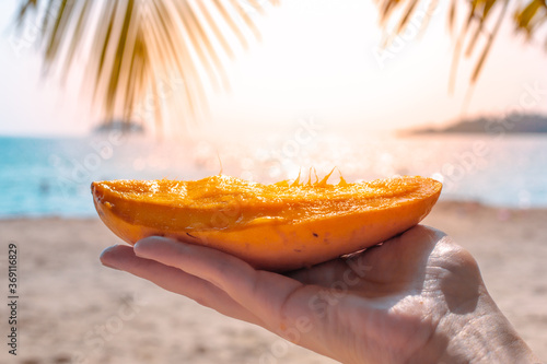Soft juicy ripe sweet yellow mango in sunlight on the background of the sea. Half a fruit. Tropical relaxation and enjoyment