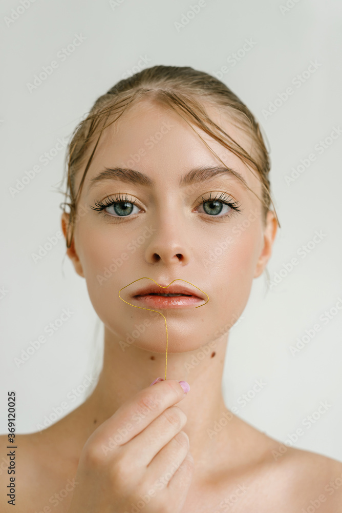 Closeup portrait of a cute blond girl with big blue eyes starring at the camera with the curl wire near the lips Closeup portrait of a cute blond girl with big blue eyes starring at the camera with the curl wire near the lips