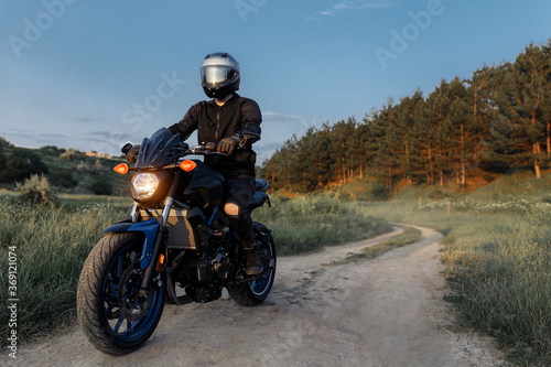 Photo of biker driving motorcycle in sunset on the country road.