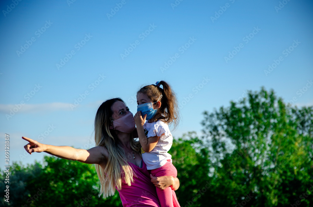 Little child with mom wearing medical masks. Mom and daughter are having fun in the summer. Kid with mom on self-isolation have a happy time Little child with mom wearing medical masks. Mom and daughter are having fun in the summer. Kid with mom on self-isolation have a happy time
