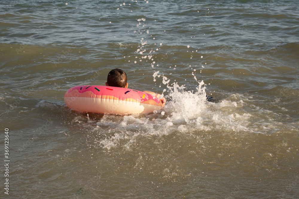 Naklejka premium A cheerful boy 5 years old swims in the sea on an inflatable ring in the form of a donut on a sunny day.