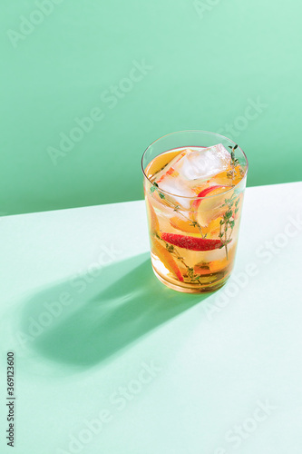 Fotografering Sparkling cold brew peach tea with thyme in glass on green paper background