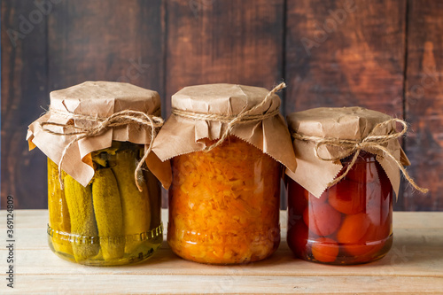 Pickled farm vegetables in glass jars on wooden background. Fermented trending food. Home rustic style.