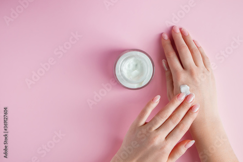 Nourishing cream and beautiful female hands on pink background. Skin care concept. Image for advertising and design.