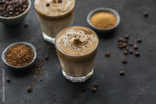 Glass of Iced Dalgona Coffee, trendy fluffy creamy whipped coffee and milk on black background.