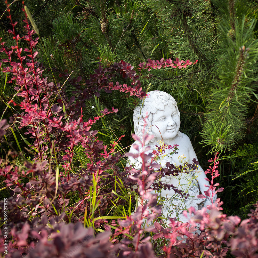 Garden sculptures in a well-kept garden. Marble sculpture of an angel Garden sculptures in a well-kept garden. Marble sculpture of an angel