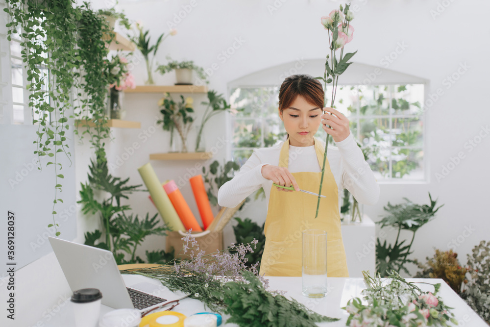 Female asian florist standing at a table in her flower workshop holding mixed flowers Female asian florist standing at a table in her flower workshop holding mixed flowers
