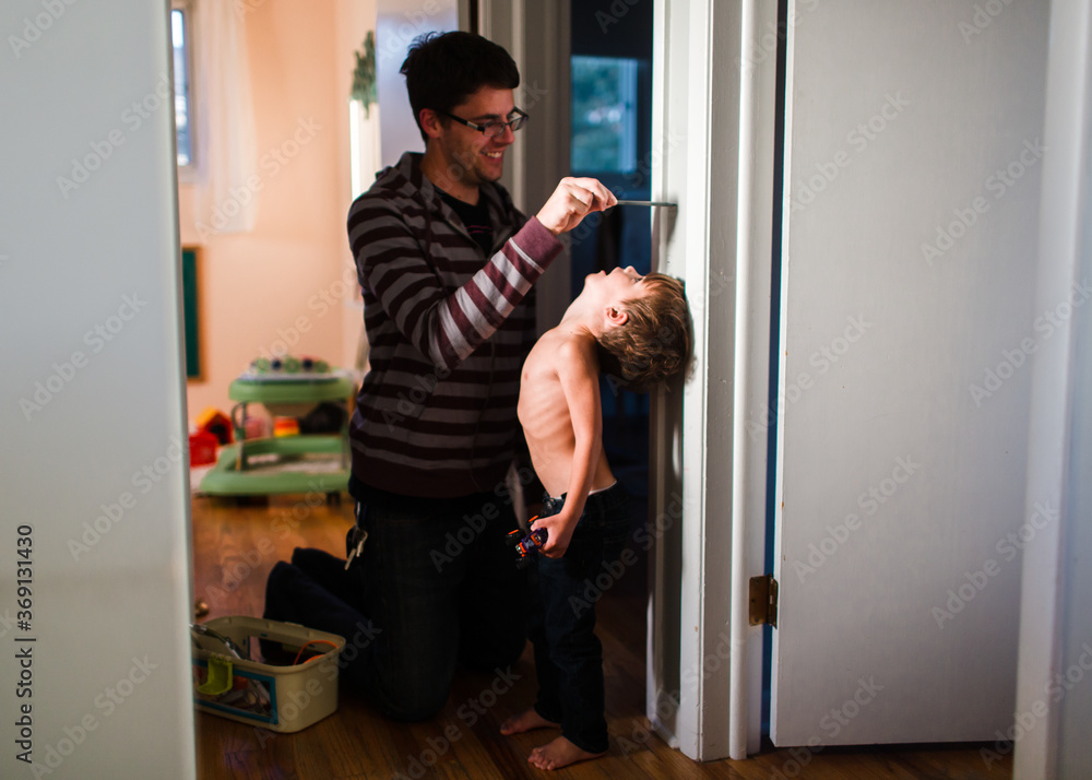 father measures sons height against wall in home father measures sons height against wall in home