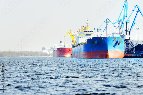 Large bulk carrier (cargo ship) in the coal terminal, close-up. Port cranes in the background. Krievu island, Riga, Latvia. Freight transportation, fuel and power generation, environmental damage photo