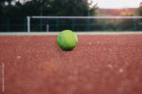 tennis ball close-up, red tennis court and net in the background