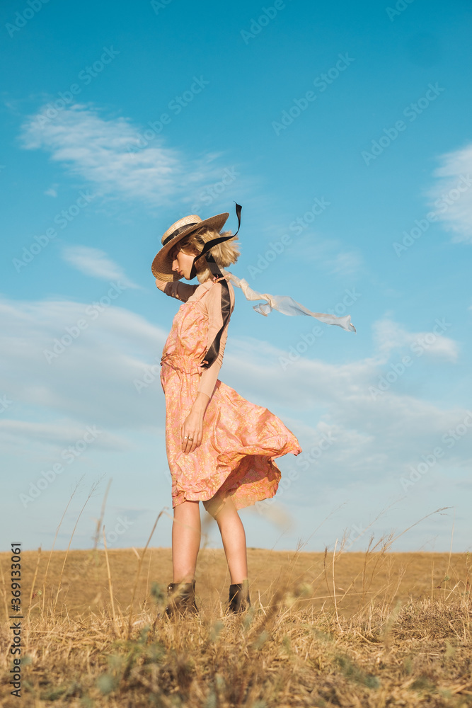 Fashionable Blond Woman Wearing Silk Dress And Sun Hat Standing In The Field Fashionable Blond Woman Wearing Silk Dress And Sun Hat Standing In The Field