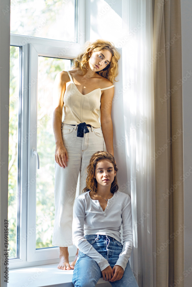 portrait of two beautiful sisters on the windowsill portrait of two beautiful sisters on the windowsill