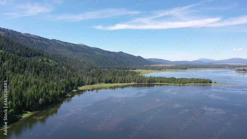 Drone aerial pan across of a beautiful lake and mountain range with luscious green trees. Drone aerial pan across of a beautiful lake and mountain range with luscious green trees.