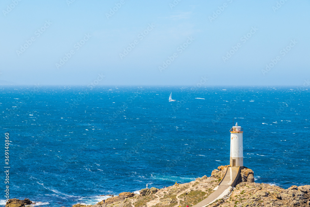 Punta Roncudo white lighthouse and the huge rough sea in the background and a sailboat sailing on the horizon